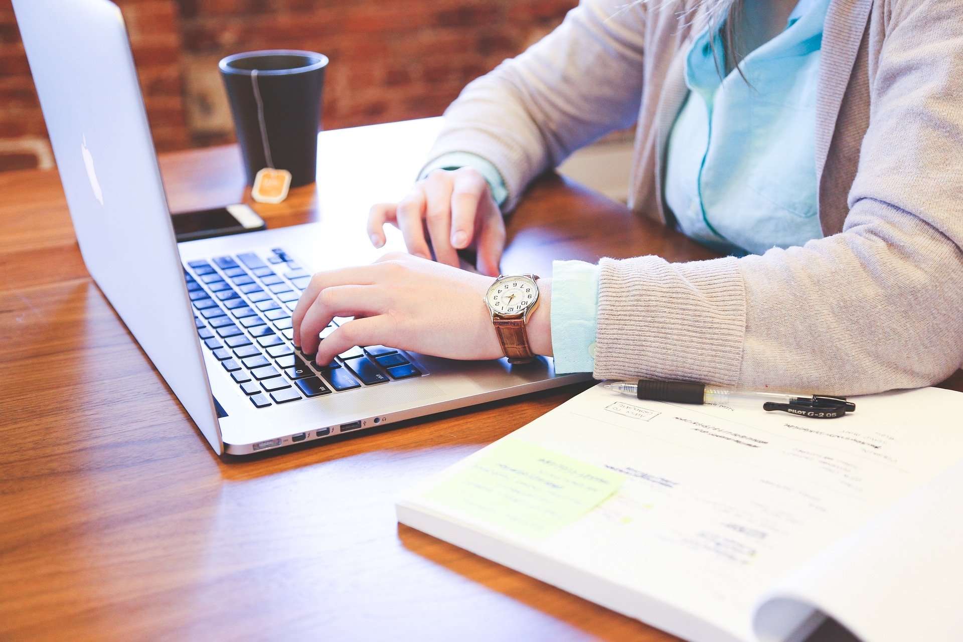 Person, die an einem Laptop arbeitet mit einer Tasse Kaffee neben sich.